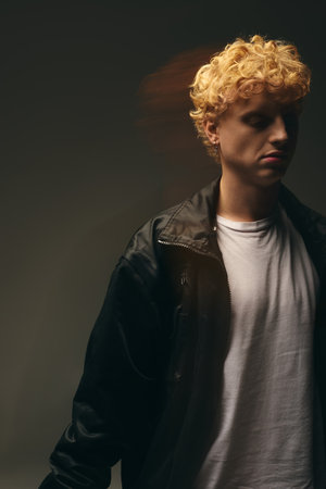 A young man presents a stylish holiday look. His outfit blends casual and festive elements, enhanced by the moody lighting that sets a sophisticated tone for the season.の写真素材