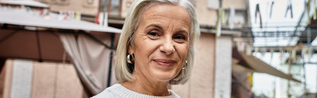 A joyful mature woman with gray hair shares a warm smile at an outdoor market atmosphere.の写真素材