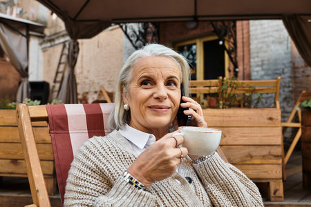 The beautiful woman with gray hair sips coffee and chats comfortably in a charming cafe.