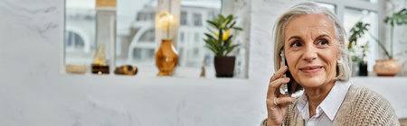 A mature woman smiles while chatting on her phone, surrounded by home decor and plants.