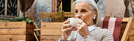 The mature woman savors her hot beverage in a cozy garden nook under soft lighting.の写真素材