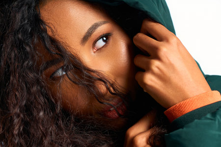 A beautiful woman with curly hair gazes thoughtfully while adjusting her cozy winter jacket.
