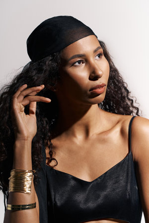 Woman with beautiful curly hair and elegant style gazes thoughtfully while softly posing.の写真素材