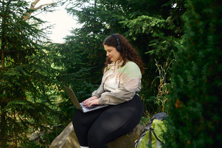 A plus size woman is deeply engaged with her laptop amid the serene beauty of nature.の写真素材