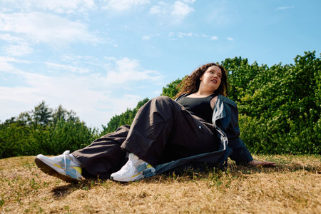 A joyful woman relaxes in a sunlit field, surrounded by lush greenery and clear skies.の写真素材