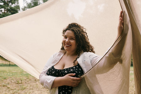 A cheerful plus size woman holds flowing fabric in a field, radiating beauty.の写真素材