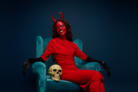 The beautiful woman, dressed in a striking red outfit, sits elegantly with a skull beside her.の写真素材