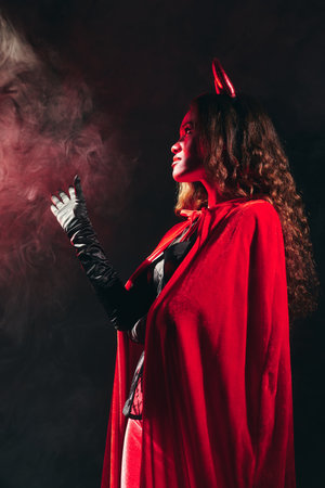 A stunning woman in a red costume embodies the Halloween spirit in dim lighting.の写真素材