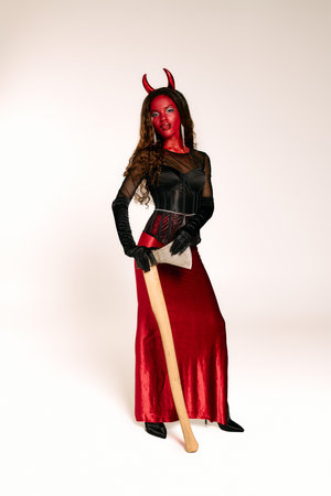 A stunning woman in a devil costume wields a bat confidently at a Halloween event.