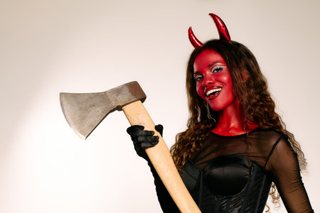 A striking woman in a devil costume with an axe enjoys Halloween celebrations with flair.