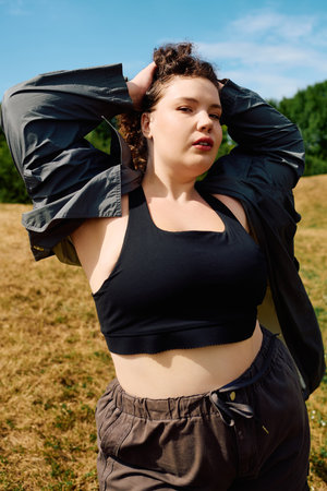 A plus size woman poses in a sunny field, confidently showcasing her style amidst natures beauty.