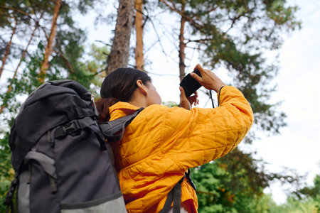 Venturing through a colorful forest, a young woman captures the radiant autumn foliage with her camera.の写真素材