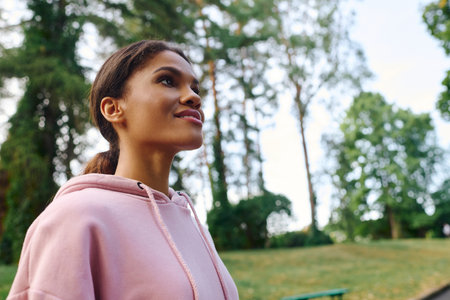 A young African American woman savors her hiking adventure in a beautiful autumn forest, embracing...
