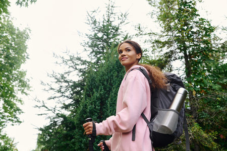 A young African American woman enjoys an energizing hike in a colorful autumn forest surrounded by...