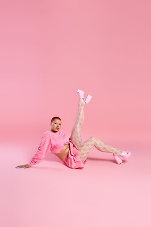 A young woman exudes confidence with pink hair and unique style, showcasing her boldness in a bright space.の写真素材