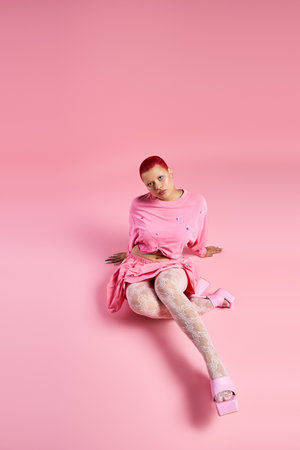 A young woman radiates boldness, sitting gracefully in a pink outfit against a matching backdrop.の写真素材