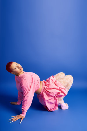 A confident young woman with short pink hair models her striking outfit in a bright studio setting.の写真素材
