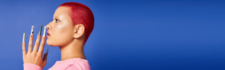 A stylish young woman with short pink hair showcases bold fashion and piercing in an artistic studio.の写真素材