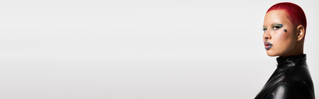 This striking young woman showcases her bold style with short pink hair and unique accessories in a studio.の写真素材