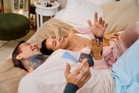 Young couple shares laughter and joy together while relaxing on their comfortable bed.の写真素材
