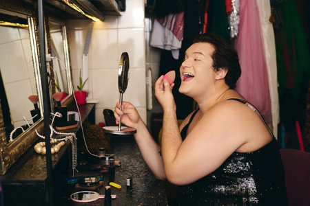 A drag queen applies vibrant makeup in a bustling backstage dressing room before a holiday show.の写真素材