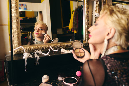 A drag queen artfully applies makeup in front of a mirror, readying for a festive show.の写真素材