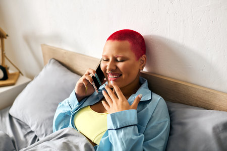 Radiating happiness, the woman relaxes in bed while chatting on her smartphone, enjoying her day.