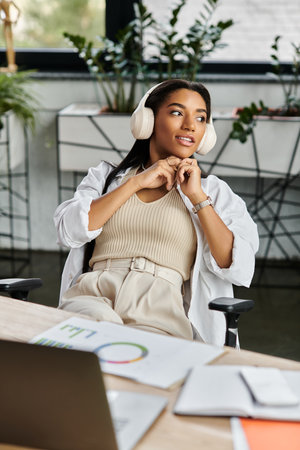 A young woman relaxes in her chair, adjusting her headphones while working in a stylish office.の写真素材