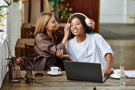 A smiling African American woman in braids enjoys a playful moment with her girlfriend at a cafe.の写真素材