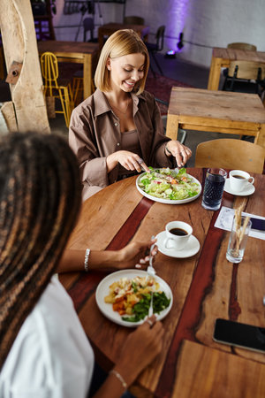 A joyful moment unfolds as an African American woman shares a lunch date at a cafe with her girlfriend.の写真素材