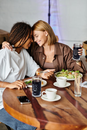 A multicultural couple smiles affectionately, sharing a cozy lunch at a cafe, radiating love and happiness.の写真素材