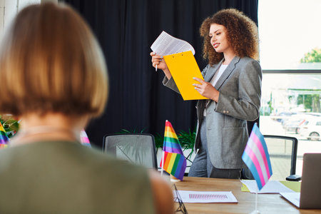A woman passionately presents LGBTQ initiatives to her engaged coworkers in the office.の写真素材