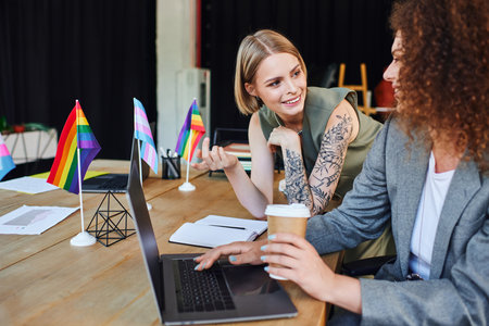 Two coworkers share ideas in a lively workspace adorned with pride flags and creativity.の写真素材