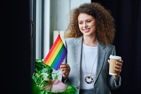 A coworker holds a rainbow flag with a smile and coffee, embracing inclusion and diversity.の写真素材