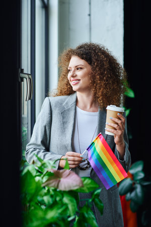 A coworker enjoys a moment by the window, proudly holding a rainbow flag and coffee.の写真素材
