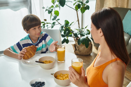 A little boy happily engages with his mother during breakfast, sharing moments over food and juice.の写真素材