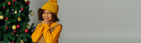 Smiling girl in yellow sweater and hat enjoys festive moments near a decorated Christmas tree