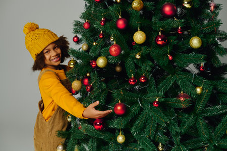 girl smiles while placing colorful ornaments on a Christmas tree for the holiday.の写真素材