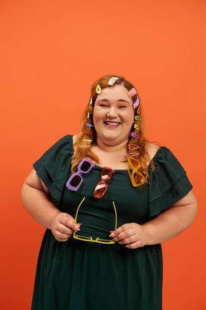A cheerful woman in a green dress holds stylish sunglasses, adorned with playful hair clips.の写真素材