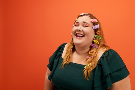 A joyful woman with colorful hair clips beams with happiness against a bold orange background.