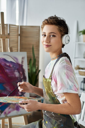 A young woman with natural makeup immersed in painting happily expresses her creativity in a cozy room.の写真素材