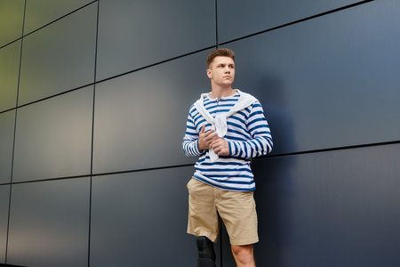 A young man wearing a striped shirt leans against a sleek wall, exuding determination and style.