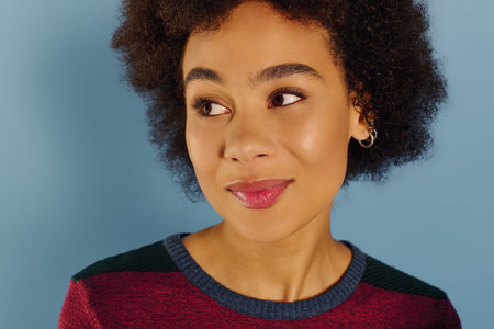 A young woman with curly hair conveys a mix of emotions while looking thoughtfully to the side.