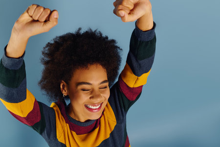 A young emotional woman celebrates with raised fists, her joy radiating in a vibrant setting.の写真素材