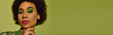 A young woman shows her emotions with bold green makeup against a bright background.