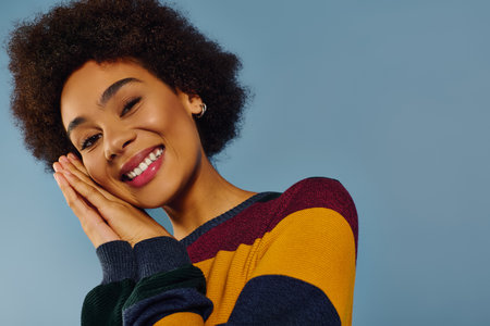 A young woman shares her joy, playfully resting her face in her hands while smiling brightly.