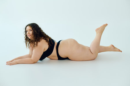 A plus size woman exudes confidence as she poses on her stomach, showcasing her beauty and curves.の写真素材
