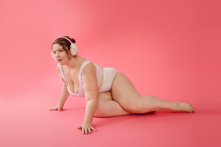 A confident plus size woman poses gracefully on a pink backdrop, showcasing her charm and style.の写真素材