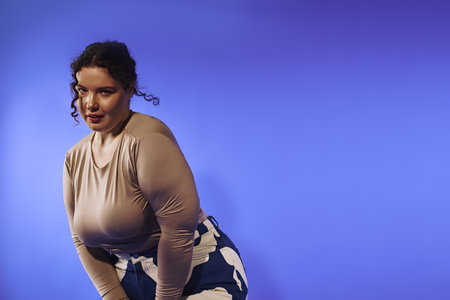 A plus size woman showcasing her unique style against a vivid blue backdrop, radiating confidence.