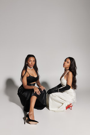 Two fashionable young women showcase their style while seated in a modern studio environment.の写真素材